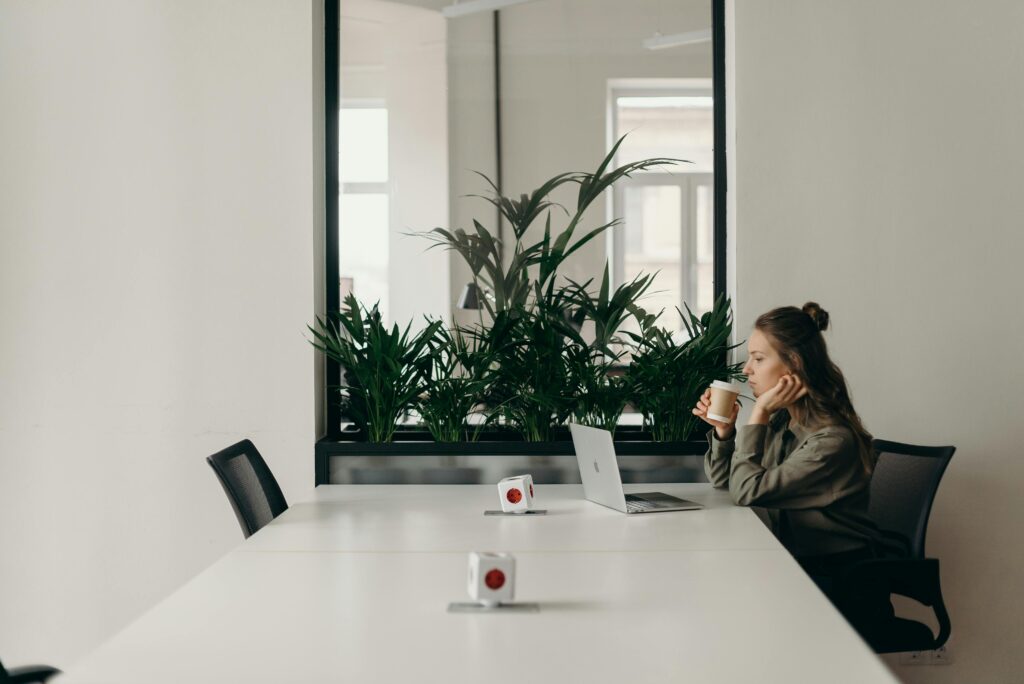 Woman working on laptop while drinking coffee in a modern, minimalist office setting.